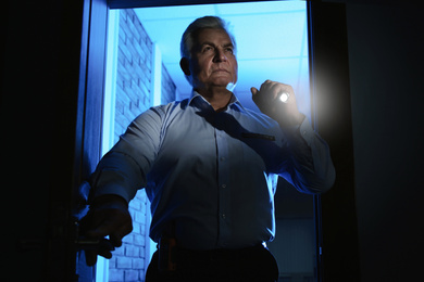 Professional security guard with flashlight checking dark room