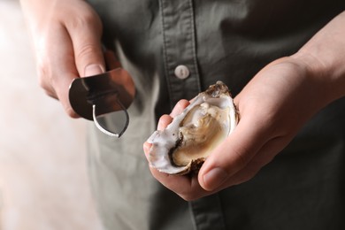 Man holding fresh oyster and knife on beige background, closeup