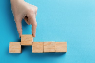 Woman arranging blank wooden cubes on light blue background, top view. Space for text