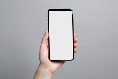 Photo of Woman holding smartphone with blank screen on grey background, closeup. Mockup for design
