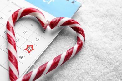 Saint Nicholas Day. Heart shape frame of candy canes and calendar with marked date December 19 on snow, closeup