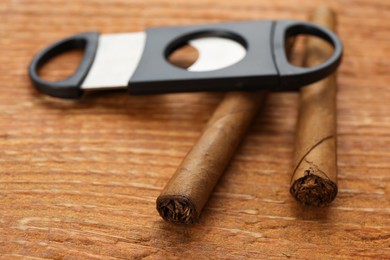 Cigars and guillotine cutter on wooden table, closeup