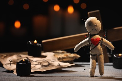 Voodoo doll pierced with pins and ceremonial items on wooden table against blurred background