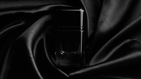 Luxury bottle of perfume on black silk, top view