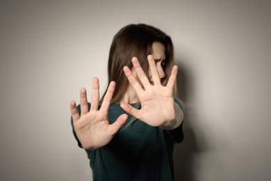 Young woman making stop gesture against light background, focus on hand