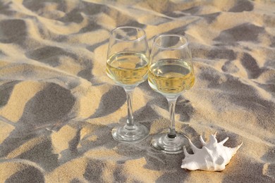 Photo of Glasses of tasty wine and seashell on sand, space for text