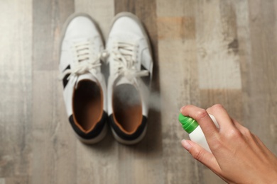 Woman spraying deodorant over pair of shoes at home, closeup