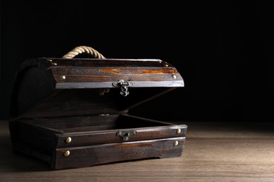 Empty treasure chest on wooden table against black background. Space for text
