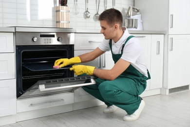 Male janitor cleaning oven tray with sponge in kitchen