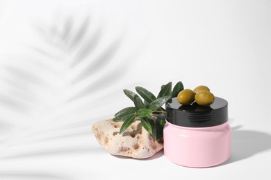 Photo of Jar of natural cream, stone and olives on white background, space for text. Cosmetic products