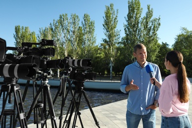 Young journalist interviewing man near river on sunny day