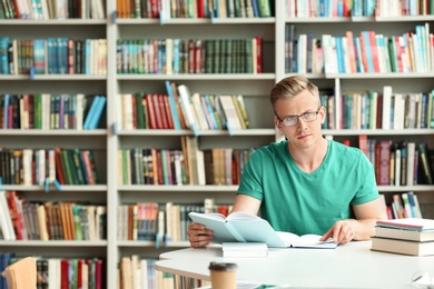 Pensive young man with books at table in library. Space for text