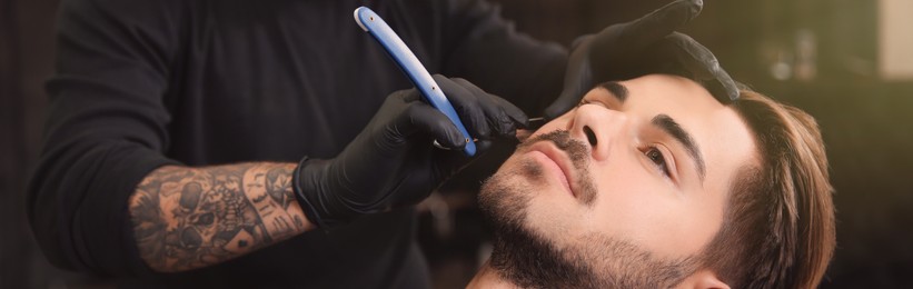 Professional hairdresser shaving client with straight razor in barbershop. Banner design