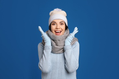 Excited woman wearing warm sweater, gloves, scarf and hat on blue background. Winter season