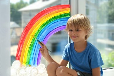 Little boy drawing rainbow on window indoors. Stay at home concept