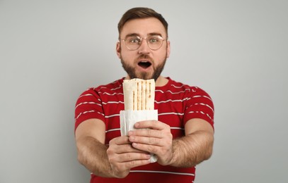 Photo of Emotional young man with delicious shawarma on grey background