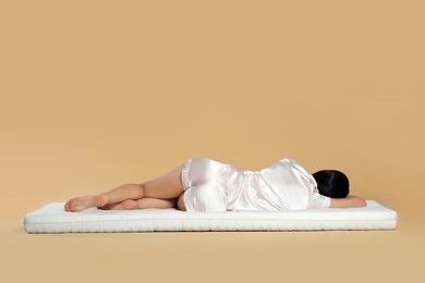Photo of Young woman lying on soft mattress against beige background, back view