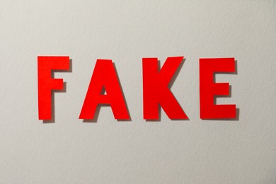 Word Fake made of red letters on grey background, flat lay