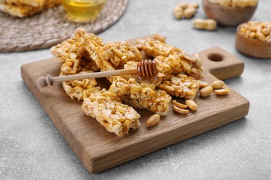 Photo of Delicious peanut kozinaki bars and honey dipper on light gray textured table