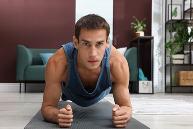 Handsome man doing plank exercise on floor at home