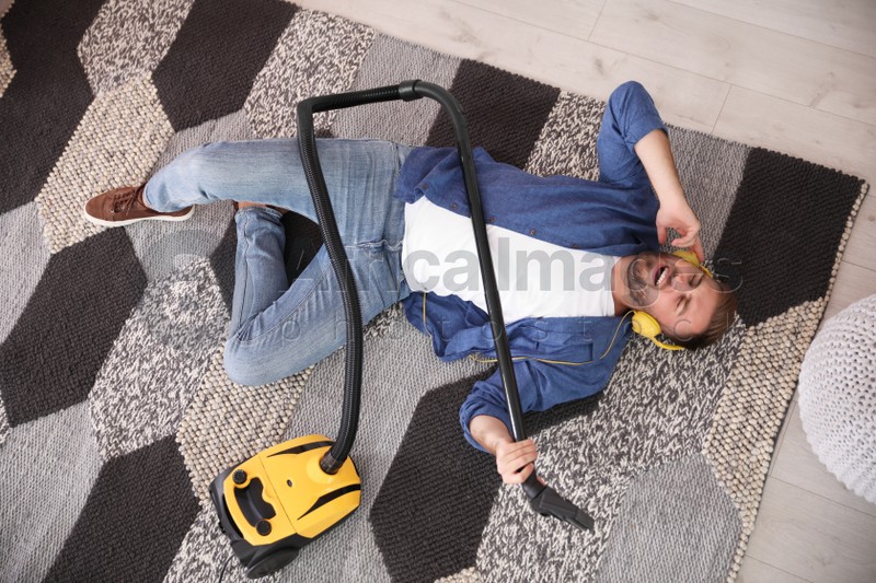 Young man having fun while vacuuming at home, above view