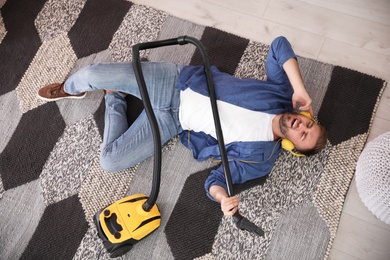 Young man having fun while vacuuming at home, above view