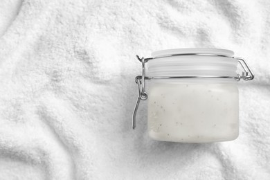 Jar of salt scrub on white towel, top view. Space for text