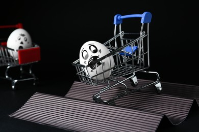 Photo of Egg with drawn scared face in shopping cart stunting on black background