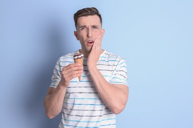 Young man with sensitive teeth and cold ice cream on color background