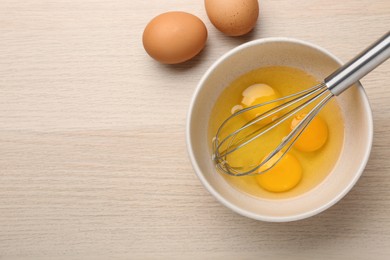 Whisk and eggs in bowl on wooden table, flat lay. Space for text