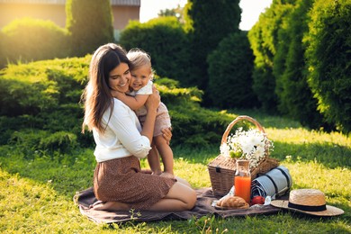 Mother and her baby daughter hugging while having picnic in garden on sunny day