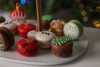 Beautifully decorated Christmas macarons on white table against blurred festive lights, closeup