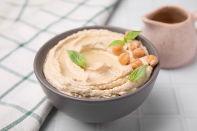 Delicious hummus with chickpeas served on white tiled table, closeup