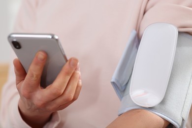 Woman checking blood pressure with modern monitor and smartphone indoors, closeup