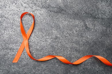 Orange ribbon on grey table, top view with space for text. Multiple sclerosis awareness