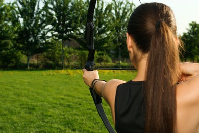 Woman with bow and arrow practicing archery in park, back view
