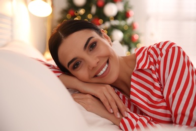 Young woman lying on bed in room with Christmas tree