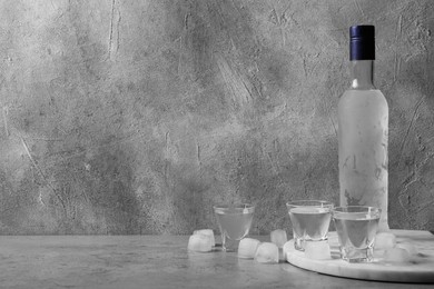 Photo of Bottle of vodka and shot glasses with ice cubes on table against grey wall. Space for text