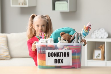 Cute little girl holding donation box with toys at home