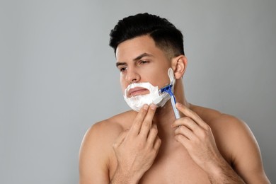 Handsome man shaving with razor on grey background