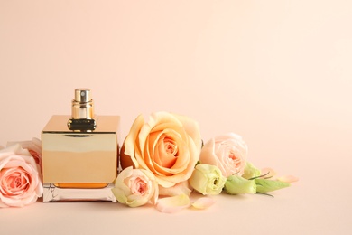 Bottle of perfume with fresh flowers on beige background, space for text