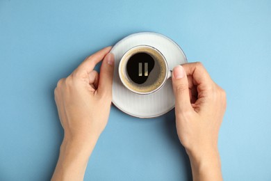 Coffee Break. Woman with cup of americano on light blue background, top view