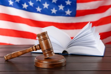 Judge's gavel and book on wooden table against American flag