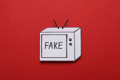 Photo of Paper TV with word Fake on red background, top view. Information warfare concept