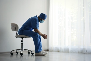 Exhausted doctor sitting on chair indoors, space for text. Stress of health care workers during COVID-19 pandemic