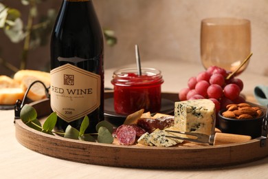 Bottle of red wine and delicious snacks on wooden table, closeup