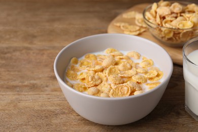 Tasty cornflakes with milk in bowl on wooden table, space for text