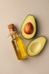 Photo of Glass bottle of cooking oil and fresh avocados on light grey background, flat lay