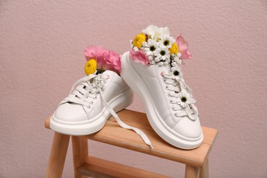Shoes with beautiful flowers on wooden stand against pale pink background