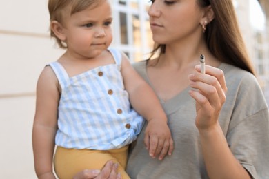 Photo of Mother with cigarette and child outdoors, focus on hand. Don't smoke near kids
